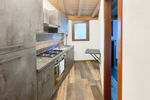 Une cuisine de taille réduite, équipée d’une cuisinière à gaz, d’un four et d’une fenêtre située au-dessus de l’évier.