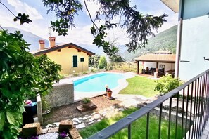 Ein Garten mit Swimmingpool, einer Holzterrasse und einem Haus mit rotem Dach.