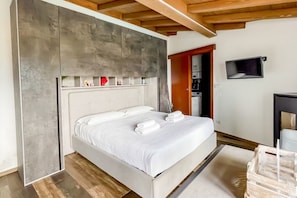 Ein modernes Schlafzimmer mit einem großen Bett, einer Holzbalkendecke und einem an der Wand befestigten Fernseher.