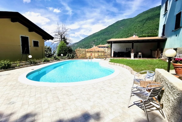 Piscina com deck revestido, área de estar externa e montanhas ao fundo.