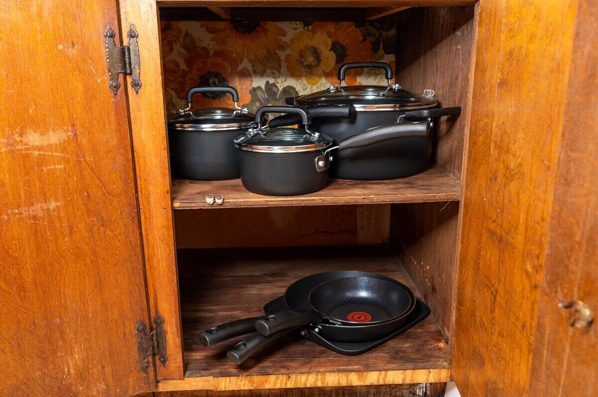 A wooden cabinet with shelves holding black pots and pans.