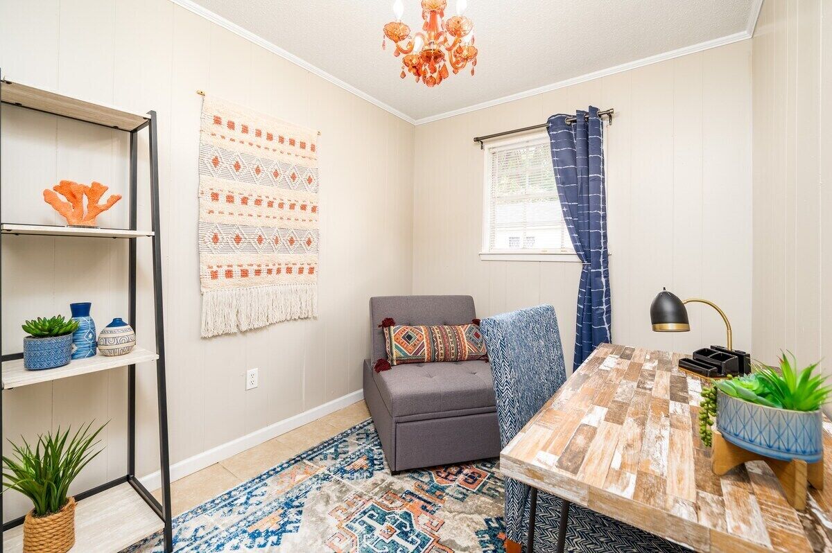 A cozy room with a grey armchair, a patterned rug, a wooden coffee table, and a shelf with decorative items.