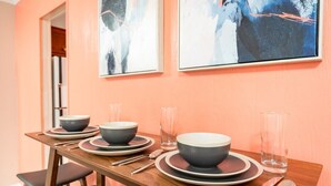 Une table à manger dressée avec des bols, des assiettes et des couverts, et des tableaux abstraits accrochés au mur.
