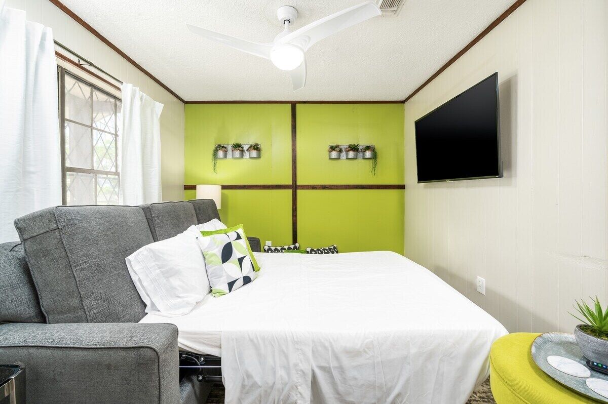Een hotelkamer met een bed, een grijze bank, een kleine tafel met een plant en een televisie aan de muur.
