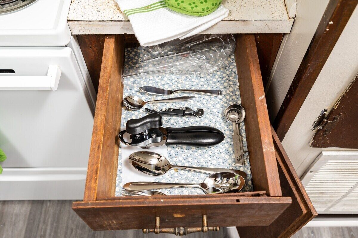 A drawer with various kitchen utensils including a can opener, spoons, and a spatula.
