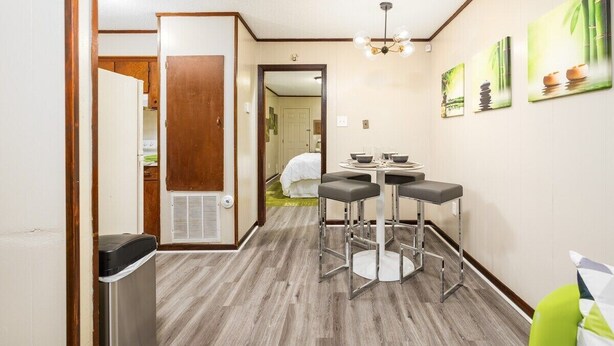 A hotel room with a wooden door, a small kitchenette, a dining area with a round table and bar stools, and a wall with framed artwork.