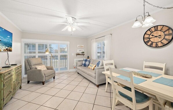 A living room with a sofa, dining table, chairs, a ceiling fan, and a clock.