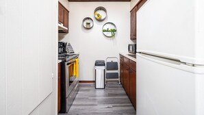 Eine kleine Küche mit Kühlschrank, Herd und Spüle. Drei Wanddekorationen und ein Mülleimer sind vorhanden.