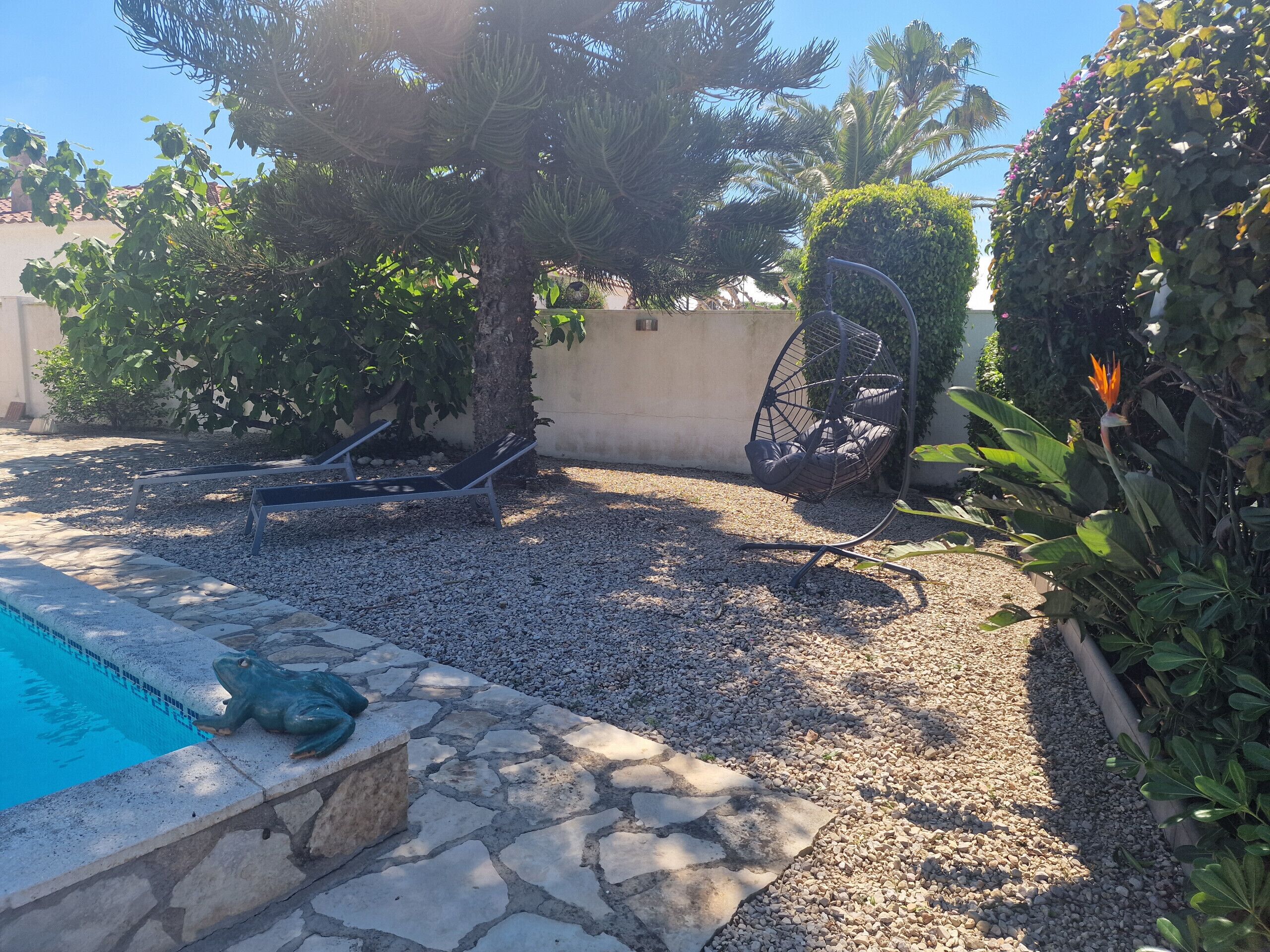 Ein Poolbereich mit einer Froschstatue, einer Hängematte und einem mit Kieselsteinen bedeckten Boden.