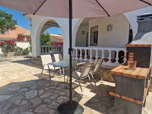 An outdoor patio with stone flooring, a glass table, and chairs under a large umbrella.