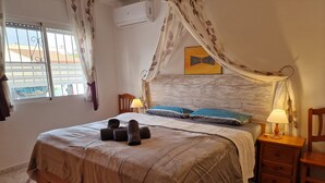 Un lit bien fait, avec une tête de lit, deux tables de chevet avec des lampes, une fenêtre avec des rideaux et un appareil de climatisation fixé au mur.