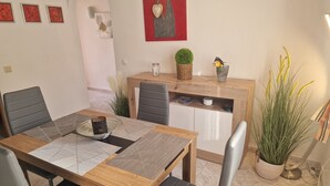 Un coin repas comprenant une table en bois, des chaises à revêtement gris, une petite plante en pot et un élément décoratif mural.
