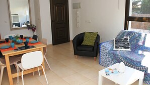 Un coin repas avec une table dressée pour quatre personnes, un fauteuil noir agrémenté d’un coussin à motifs et une fenêtre donnant sur un paysage verdoyant.