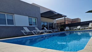 Une piscine entourée de chaises longues blanches et dotée d’un espace salon abrité.