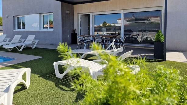 Un bâtiment moderne doté d’un espace extérieur couvert avec des sièges, d’une piscine et d’une pelouse bien entretenue.