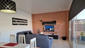 Un salon moderne comprenant un canapé, un téléviseur et un coin repas avec une table et des chaises.