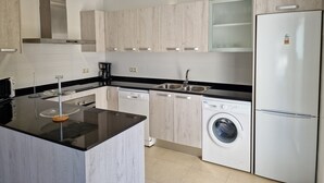 Une cuisine moderne dotée d’un îlot central, d’appareils électroménagers intégrés et de meubles de cuisine en bois clair.