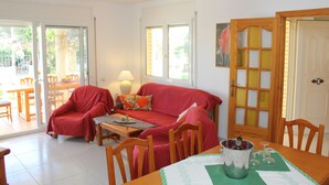 A living room with a red sofa, a wooden dining table with chairs, and a glass door with a wooden frame. - "Maria Luise"@MARISOL: 600m to the beach, private pool, A/C, WiFi, dog beach. (Riumar)