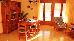 Uma sala de jantar com uma mesa e cadeiras de madeira, um lustre e vista através de grandes janelas.