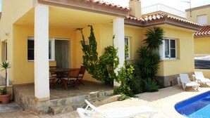 Un edificio amarillo con un patio cubierto, piscina y mobiliario exterior.
