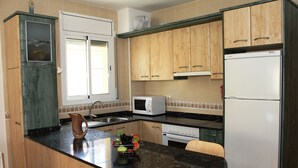 Una cocina con armarios de madera, microondas, refrigerador, pileta y un frutero sobre la encimera.