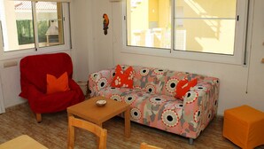 Una habitación con sofá, una silla roja, una mesa de madera y una ventana con vista a un edificio.