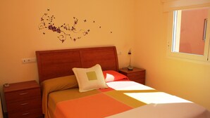 A bedroom with a wooden headboard, a single bed with an orange and white bedspread, a nightstand with a lamp, and a wall decoration of flowers and butterflies. - "Mireli"@MARISOL: 300m to the beach, private pool, A/C, WiFi, dog beach. (Riumar)
