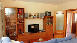 A living room with a blue sofa, wooden entertainment unit, and a television. - "Mireli"@MARISOL: 300m to the beach, private pool, A/C, WiFi, dog beach. (Riumar)