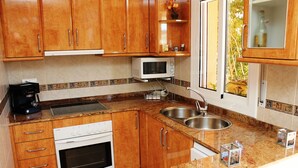 A kitchen with wooden cabinets, a microwave, a stove, a sink, and a window with a view of trees. - "Mireli"@MARISOL: 300m to the beach, private pool, A/C, WiFi, dog beach. (Riumar)