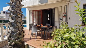 Eine Terrasse mit Tisch und Stühlen, im Hintergrund ein Pool und eine Palme.