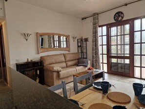 Una sala de estar con un sofá color beige, una mesa de comedor de madera y un ventanal con cortinas.