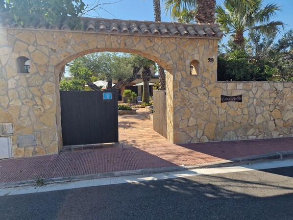 Een stenen poortboog die leidt naar een hek, een stenen muur met een bord waarop 'Casa Pedro' staat, en een verhard pad.