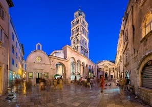 Una plaza histórica con una imponente torre campanario, una cúpula y una serie de arcos.