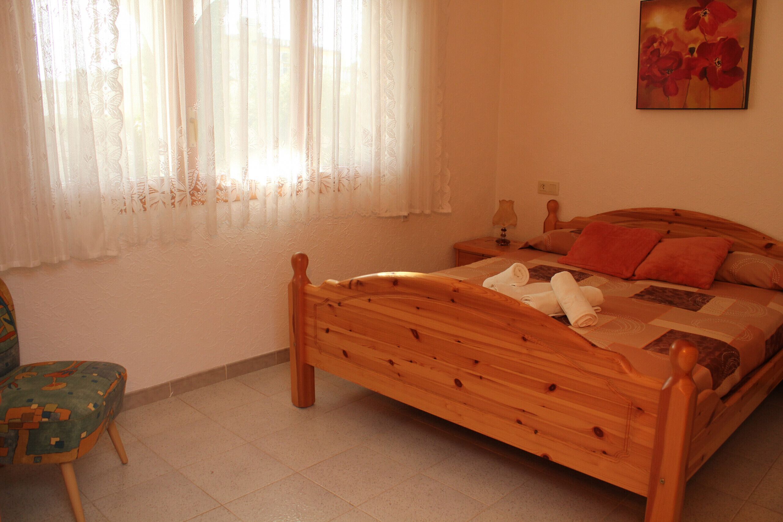 Un lit en bois avec une courtepointe, une chaise, une table de chevet et un tableau accroché au mur.
