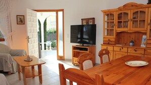 Ein Wohnzimmer mit einem Holzesstisch, Stühlen, einem Fernseher und einem Schrank.