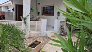Una zona patio coperta con tavolo e sedie, circondata da vasi con piante e un piccolo aiuola.
