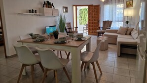 Un'area pranzo con un tavolo di legno, sedie bianche e un portatile. C'è anche un divano e una poltrona nella zona soggiorno.