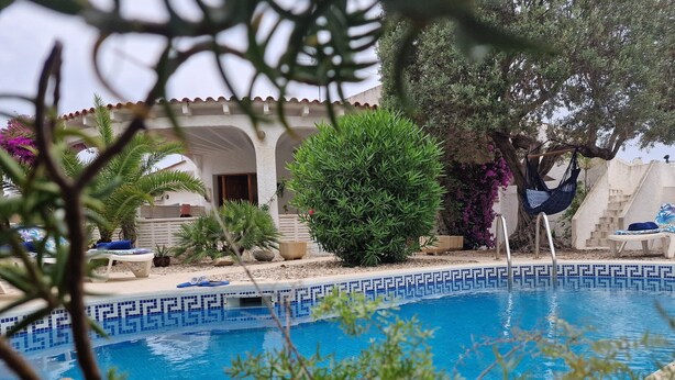 Zona piscina con bordo piastrellato, sedie a sdraio e un'amaca.