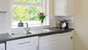 Una cocina con ventana, pileta, tetera y lavavajillas.