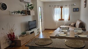 Una sala moderna con televisor, sofá, mesa de comedor y electrodomésticos de cocina.