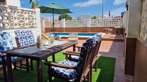 Un patio exterior con piscina, mobiliario de madera y una valla decorativa.