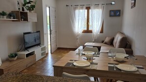 Un comedor con mesa de madera dispuesta para cuatro personas, un sofá y un televisor sobre un mueble.
