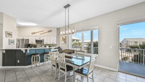 A modern kitchen with white cabinets, a central island, and a dining area with a glass table and white chairs. - Crystal View 203 3 bedroom/  3 bath unit Beach service great view SO MUCH SPACE (Miramar Beach)