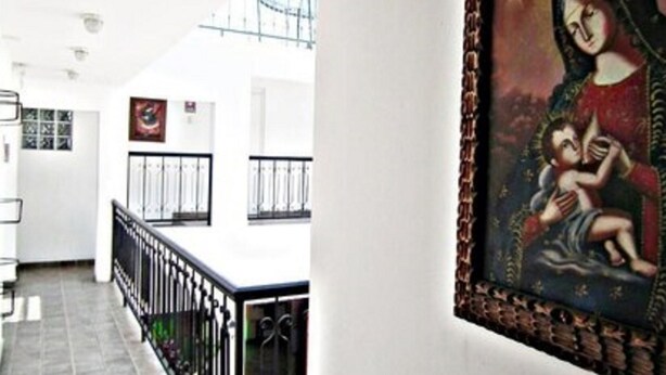 Un couloir avec un mur blanc, une rambarde noire et un tableau encadré représentant une figure religieuse.