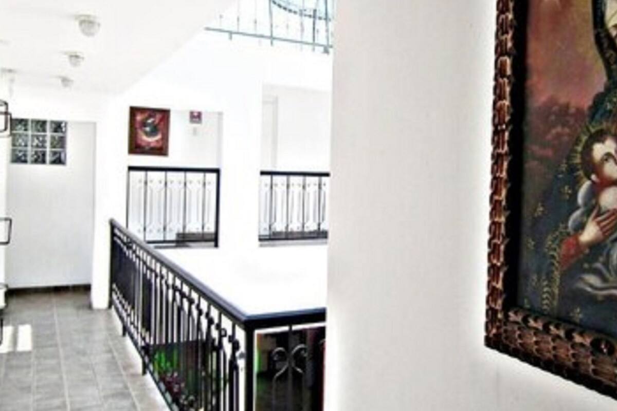 A hallway with a white wall, a black railing, and a framed painting of a religious figure.