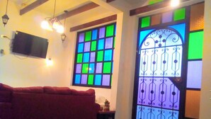 Une pièce avec un canapé rouge, un téléviseur fixé au mur et une fenêtre ornée de vitraux colorés.
