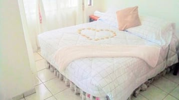 A neatly made bed with a heart-shaped quilt design, a beige pillow, and a floral-patterned skirt on the bed.
