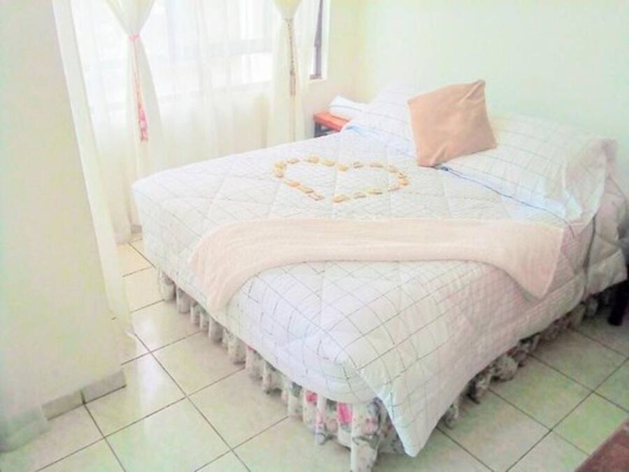 Una cama bien hecha con un edredón de diseño con forma de corazón, una almohada color beige y una falda con estampado floral.