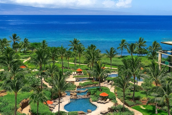 A resort with a swimming pool, palm trees, and a view of the ocean.