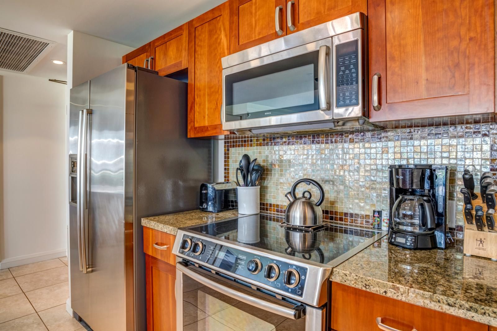A modern kitchen with stainless steel appliances, wooden cabinets, and a tiled backsplash.